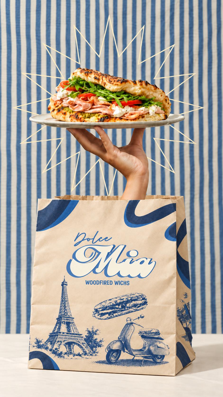 Une main surgit du vrai sac Dolce Mia et présente un panuozzo sur une assiette, devant un fond rayé bleu et crème